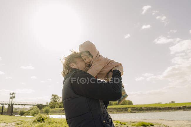 Pai nuzzling filha enquanto estava perto da margem do rio no dia ensolarado — Fotografia de Stock