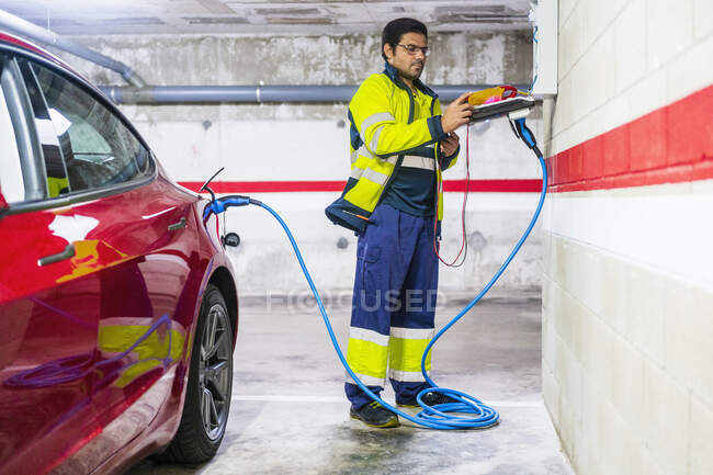 Техник-мужчина заряжает электромобиль в автомастерской — стоковое фото