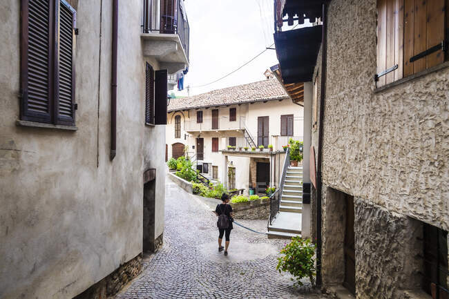 Italia, Piemonte, Turista donna in piedi nel mezzo di un vicolo di ciottoli in un antico borgo rurale — Foto stock