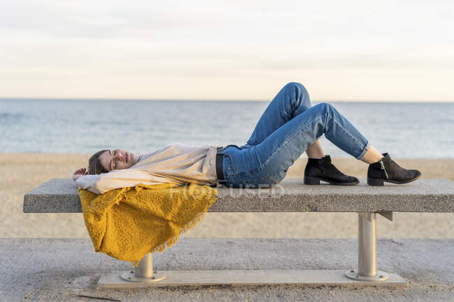 Giovane donna sdraiata sulla panchina sul lungomare durante il tramonto — Foto stock