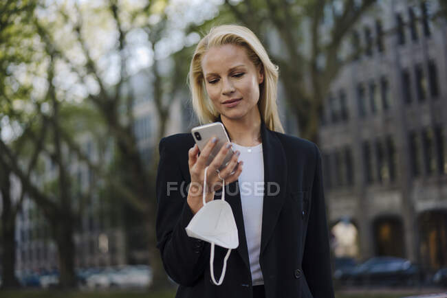 Beautiful businesswoman using mobile phone while standing in city — Stock Photo
