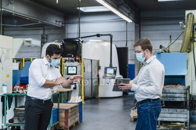 Male coworkers using digital tablet while maintaining social distancing in factory — Stock Photo