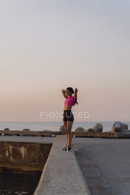 Young woman with hand in hair standing on retaining wall against sea — Stock Photo