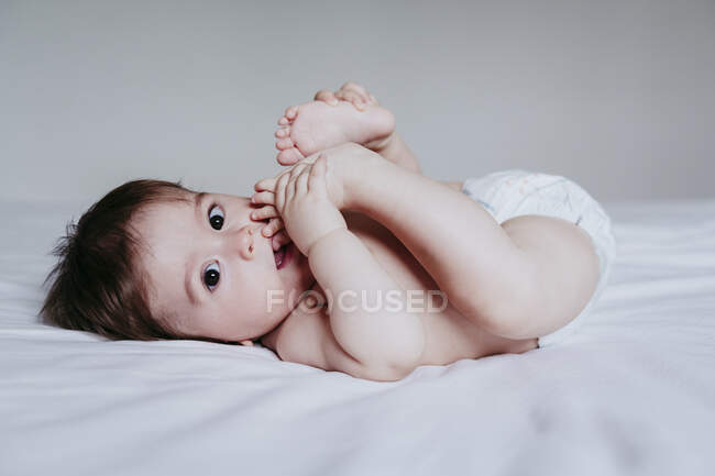 Mignon bébé garçon mettre le pied dans la bouche tout en étant couché sur le lit à la maison — Photo de stock