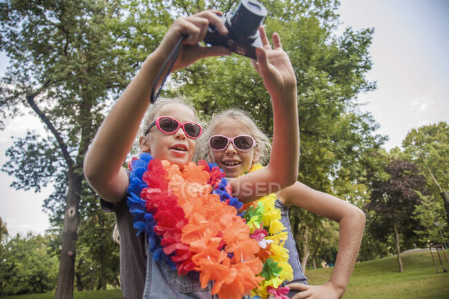 Chicas alegres en gafas de sol y guirnaldas florales con cámara en el parque - foto de stock