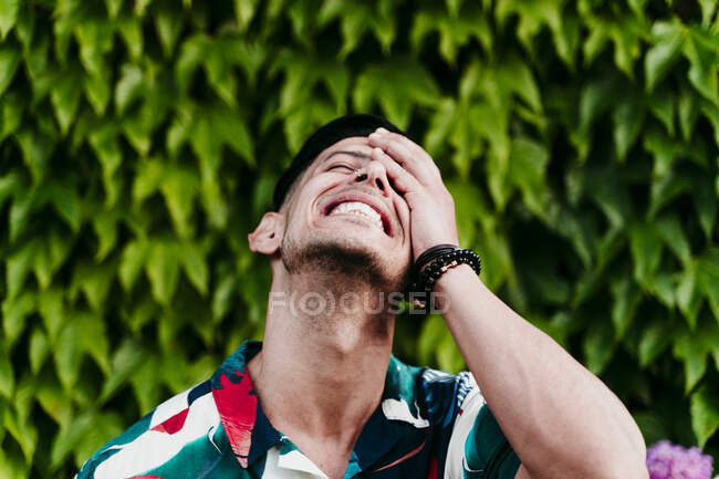 Uomo sorridente volto di copertura mentre in piedi contro siepe edera — Foto stock