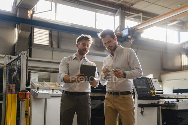 Les hommes d'affaires utilisant une tablette numérique tout en examinant l'objet métallique à l'usine — Photo de stock