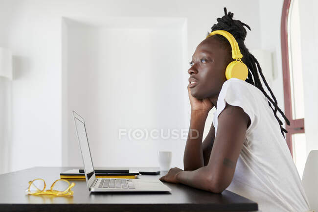 Nachdenkliche Geschäftsfrau mit Laptop am Schreibtisch trägt Kopfhörer während sie zu Hause sitzt — Stockfoto