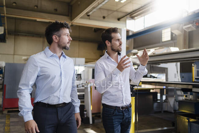 Joven hombre de negocios mirando hacia otro lado mientras discute con su colega en la fábrica moderna - foto de stock