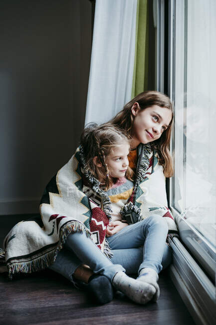 Sorella coperto a guardare attraverso la finestra mentre seduto a casa — Foto stock