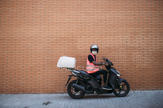 Delivery man on motorbike with protective mask delivering food — Stock Photo