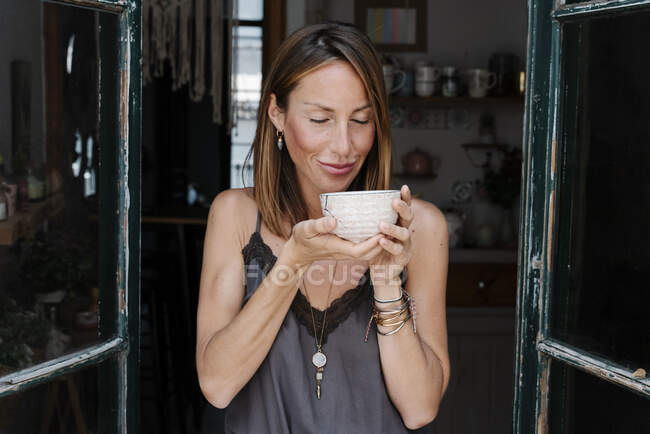 Mulher sorridente com olhos fechados segurando tigela de chá matcha no café — Fotografia de Stock