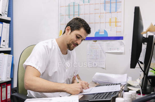 Médico varón escribiendo en el documento en el escritorio en la farmacia - foto de stock