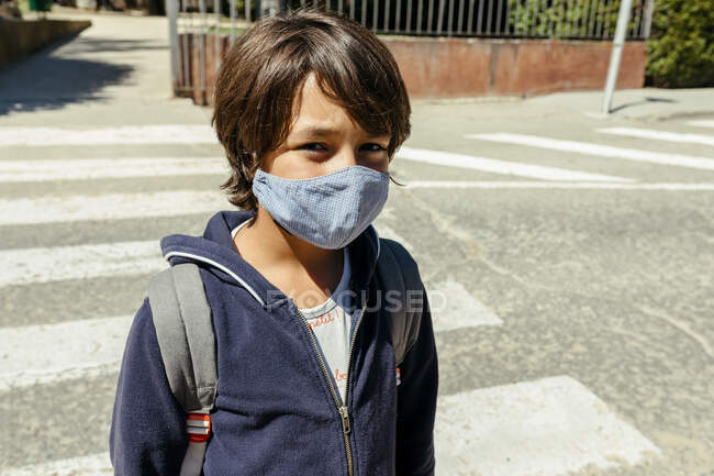 Schoolboy wearing mask standing on road during sunny day — Photo de stock