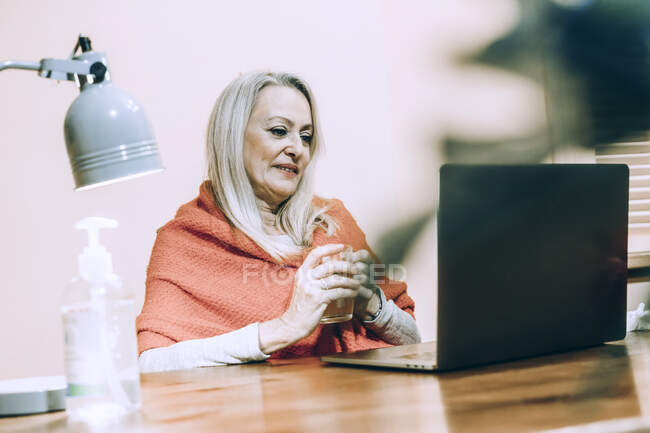 Senior mulher segurando beber vidro durante consulta on-line em casa — Fotografia de Stock