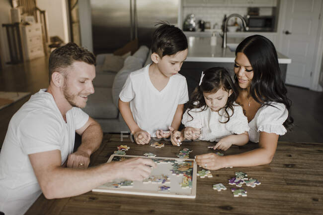 Genitori sorridenti risolvere puzzle con i bambini sopra il tavolo a casa — Foto stock