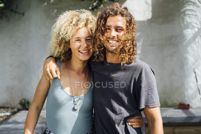 Smiling friends with arm around standing against wall — Stock Photo