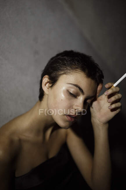 Donna con gli occhi chiusi tenuta sigaretta contro muro grigio — Foto stock
