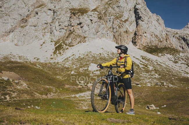 Woman with bicycle looking away against rock mountain on sunny day, Picos de Europa National Park, Cantabria, Spain — Stock Photo