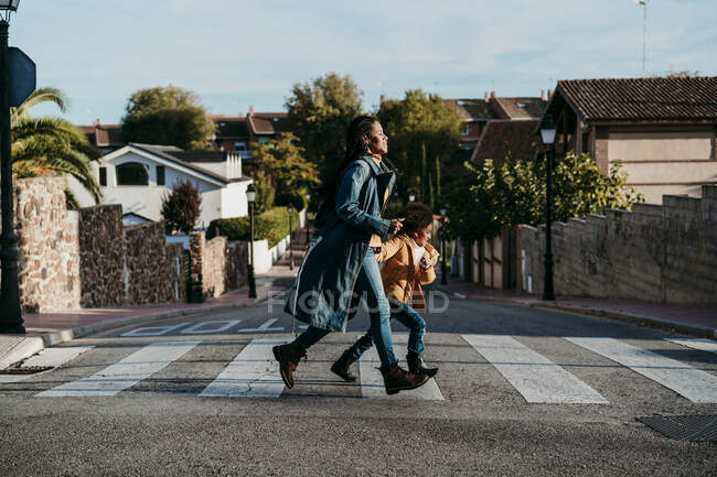 Woman and girl running while crossing road at city — Stock Photo