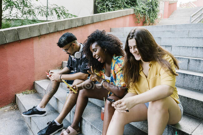 Young woman taking selfie while friends text messaging on smart phone sitting on steps — Stock Photo