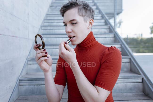 Primo piano del giovane trans che applica il rossetto mentre siede sui gradini — Foto stock