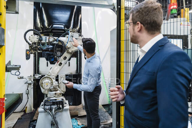 Коллеги смотрят на роботизированную руку, стоя на заводе — стоковое фото