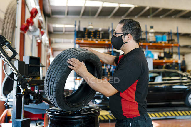 Mechaniker mit Maske untersucht Reifen in Autowerkstatt — Stockfoto
