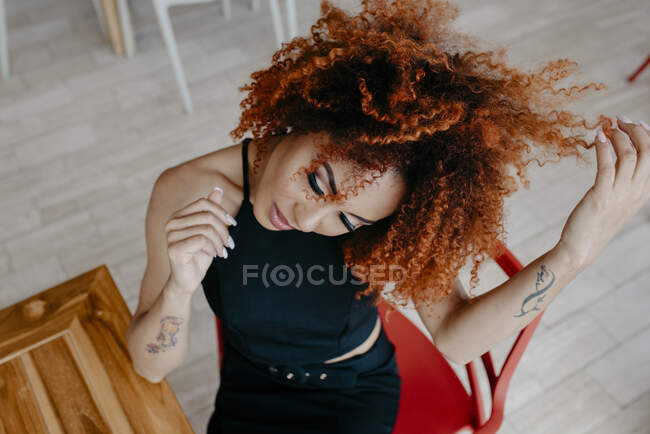 Mulher de cabelo afro com a mão no cabelo sentado na cadeira no café — Fotografia de Stock