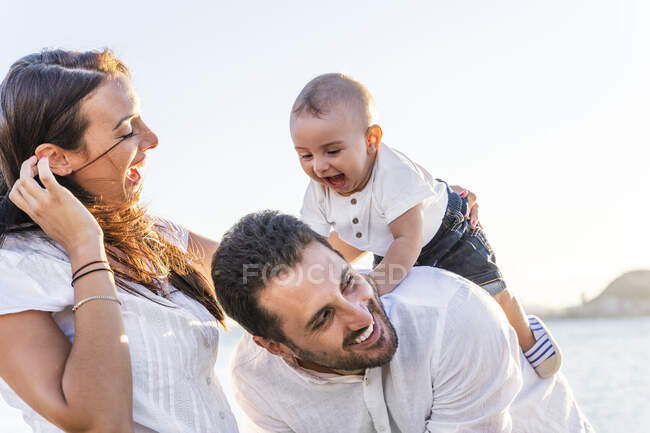 Cheerful parents playing with baby son against clear sky during sunset — Stock Photo