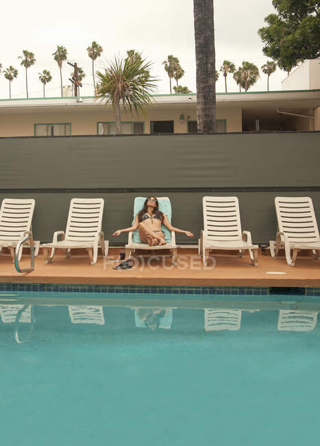 Mujer relajándose en la tumbona junto a la piscina durante las vacaciones de verano - foto de stock