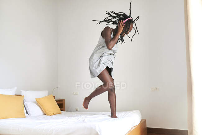 Mujer joven disfrutando bailando y escuchando música en la cama en casa - foto de stock