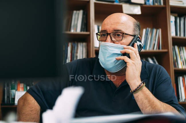 Бізнесмен у захисній масці під час розмови на смарт-телефоні під час COVID-19 — стокове фото