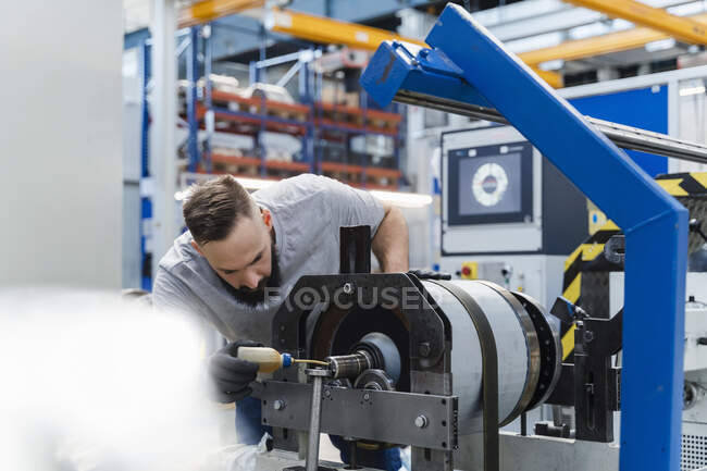 Male technician oiling machinery while examining in industry — Stock Photo