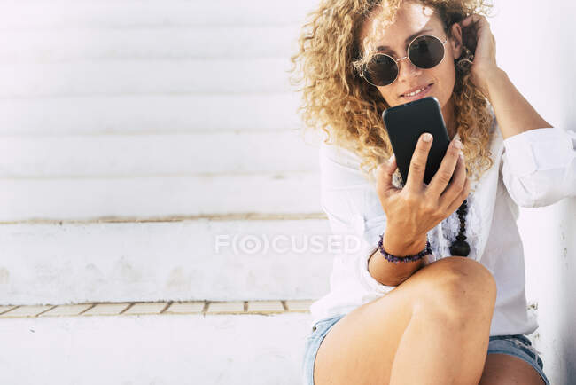 Красива жінка в сонцезахисних окулярах за допомогою смартфону сидить на сходах. — стокове фото