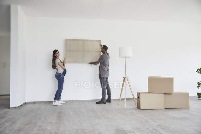 Couple accrocher le cadre sur le mur à la nouvelle maison — Photo de stock
