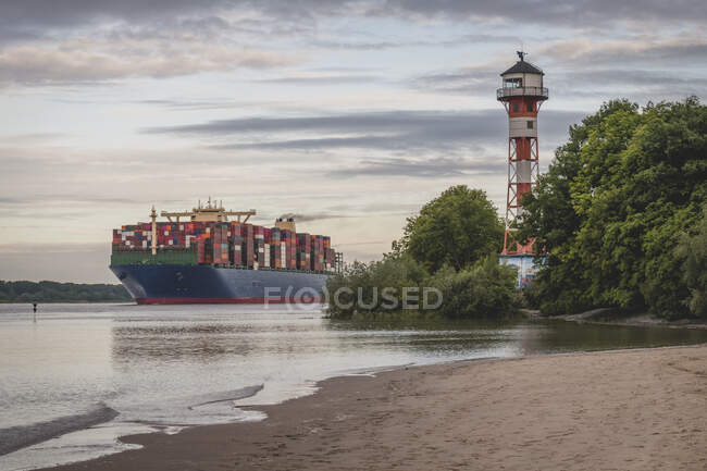 Alemania, Hamburgo, barco de contenedores en el río Elba y el faro de Wittenbergen al atardecer - foto de stock