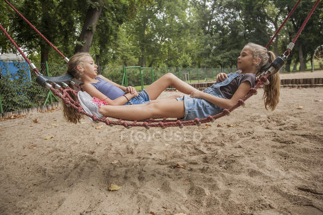 Meninas relaxantes na corda balançar no playground — Fotografia de Stock