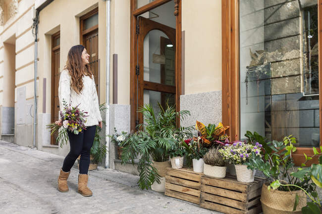 Mujer con ramo de pie y mirando a la florería - foto de stock