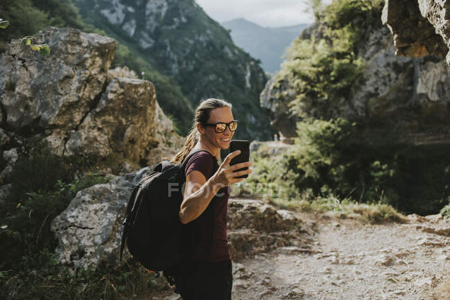 Smiling female trekker taking selfie through smart phone while hiking — Stock Photo