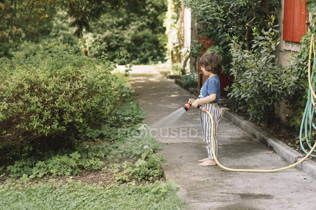 Ragazzo irrigazione piante mentre in piedi su sentiero in cortile — Foto stock
