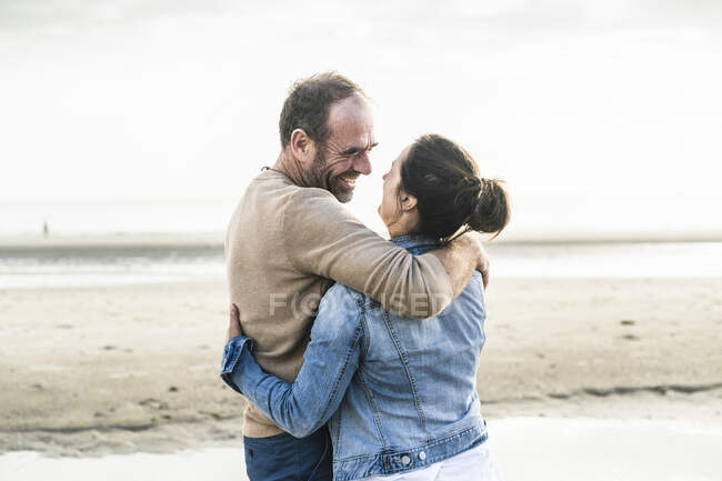 Couple joyeux embrassant tout en se tenant à la plage contre le ciel — Photo de stock