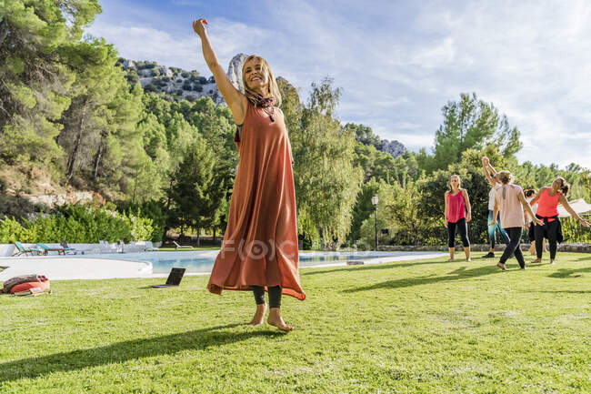 Sonriente instructora de fitness bailando con turistas en la hierba en el retiro de salud durante el día soleado - foto de stock