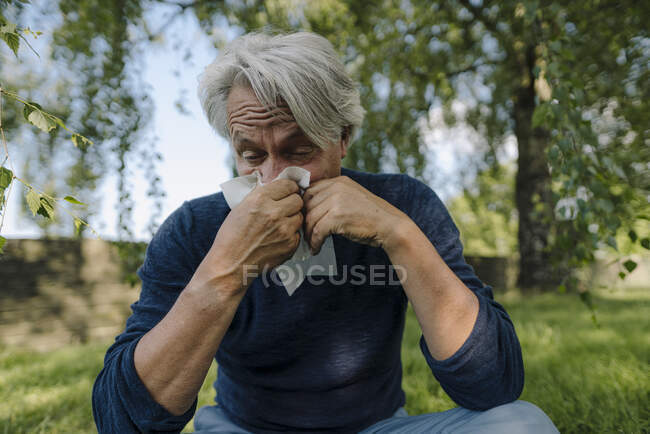 Hombre arrugado que sopla la nariz mientras está sentado en el campo - foto de stock