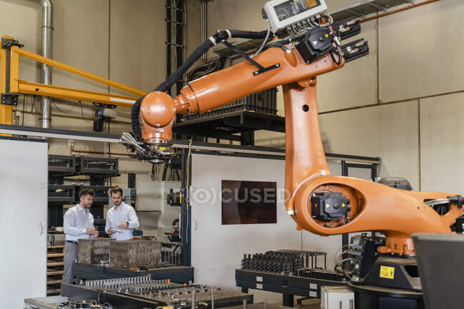 Automatische Roboterarmmaschine mit Geschäftsleuten im Hintergrund in der Fabrik — Stockfoto