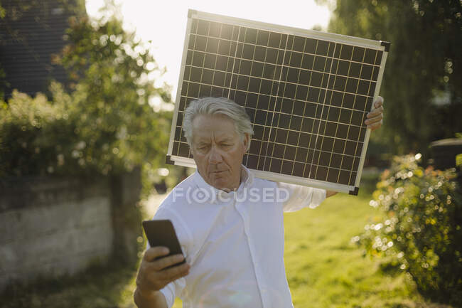 Чоловік тримає сонячну панель при телефоні на подвір 