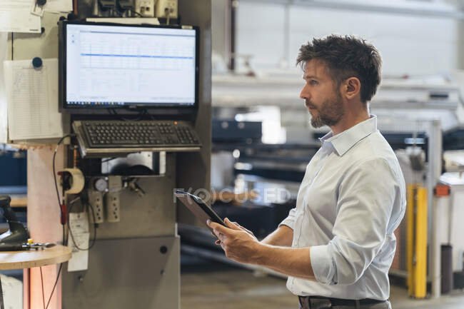 Inspector using digital tablet while standing by machine at factory — Stock Photo