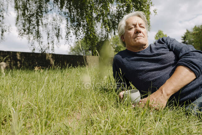 Contemplating man with cup lying on side over grass in backyard — Stock Photo