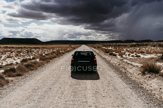 España, Navarra, Nubes de tormenta sobre coche conduciendo por camino de tierra vacío en Bardenas Reales - foto de stock