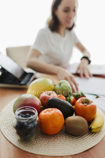 Obst auf dem Tisch mit Frau, die im Hintergrund zu Hause arbeitet — Stockfoto
